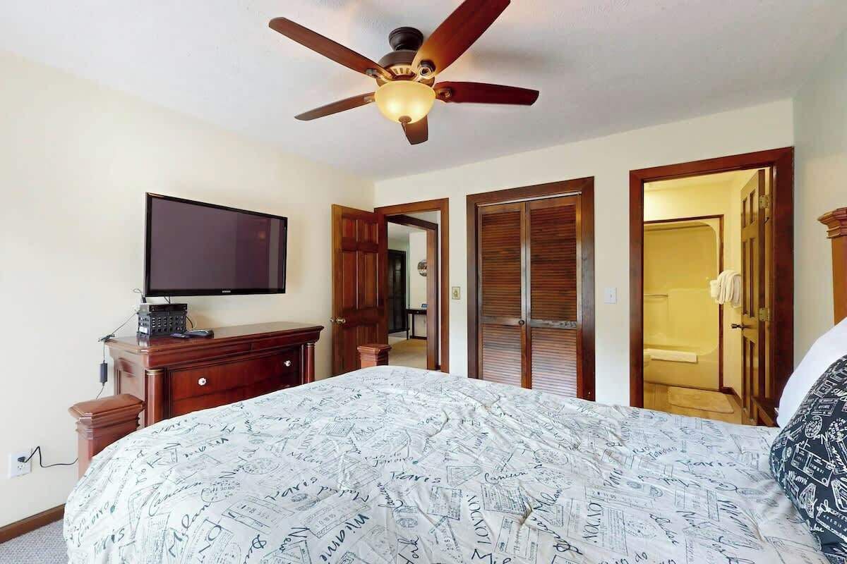 A hotel room with a bed, a television, a ceiling fan, and wooden doors.