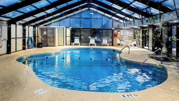 An indoor swimming pool with a glass ceiling, lounge chairs, and a lifeguard station. - Shipwatch Pointe II  P-302 (Myrtle Beach)