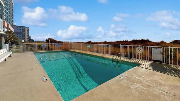 A swimming pool with a white fence, a lifebuoy, and a bench. - Summer Place Unit B-4 (North Myrtle Beach)