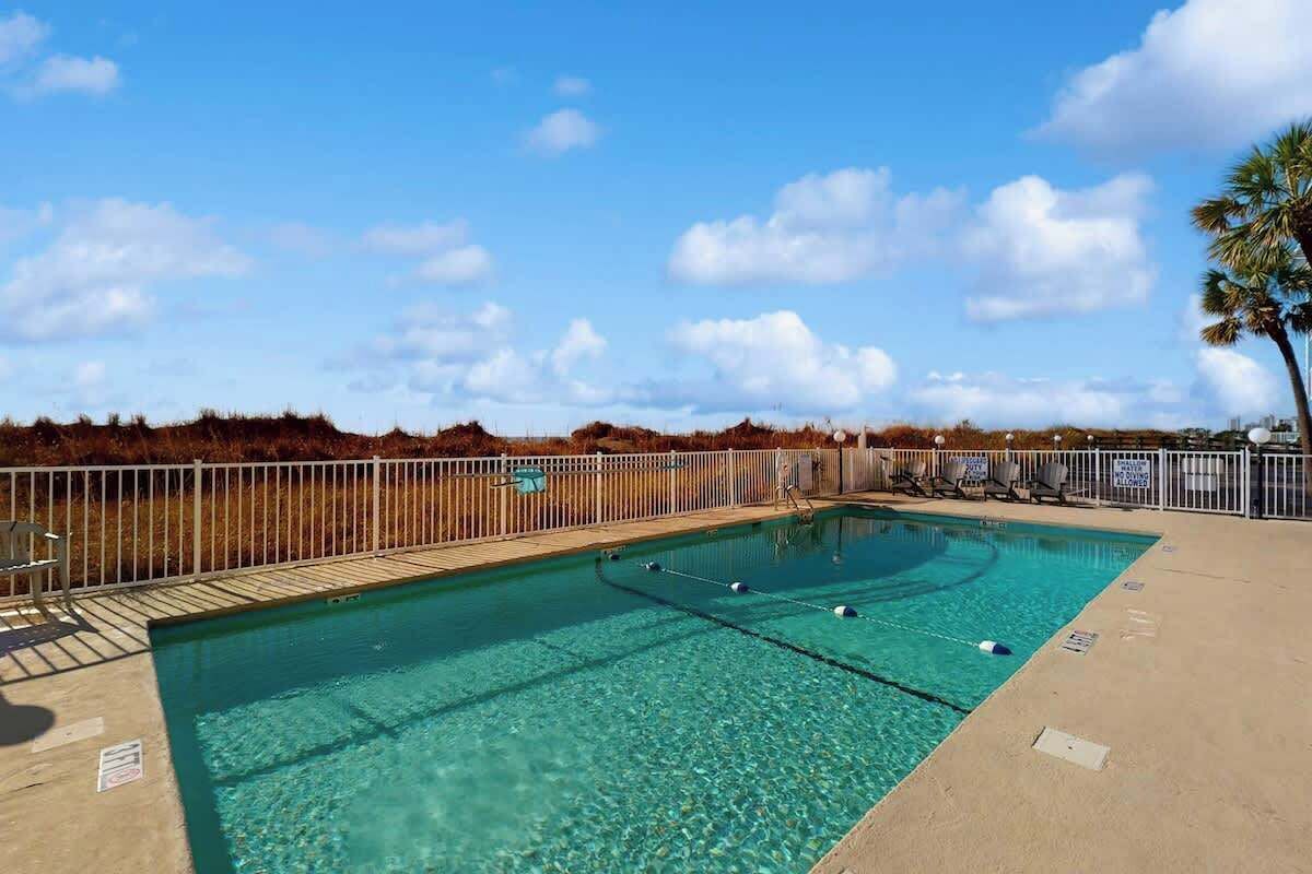 Ein klarer, blauer Swimmingpool mit umzäunter Liegeflächen, eingebettet in eine natürliche Landschaft.