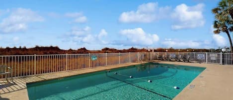 Ein klarer, blauer Swimmingpool mit umzäunter Liegeflächen, eingebettet in eine natürliche Landschaft.