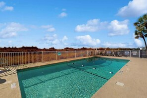 A clear blue swimming pool with a fenced deck area, surrounded by a natural landscape. - Summer Place Unit B-4 (North Myrtle Beach)