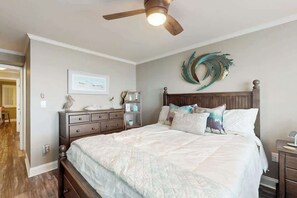 Ein Schlafzimmer mit Bett, Nachttisch, Kommode, Deckenventilator und Wanddekoration.