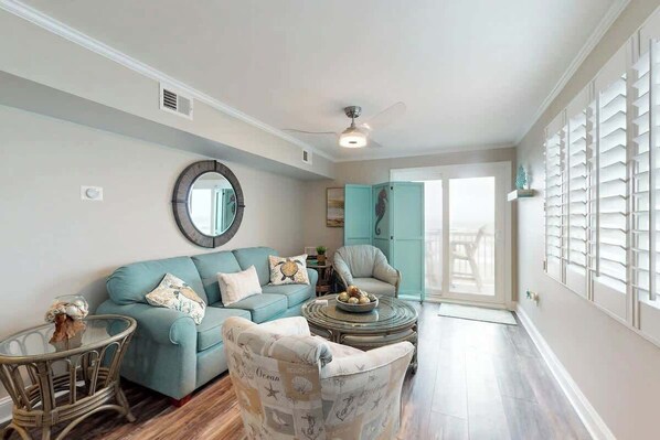 Een woonkamer met een blauwgroene bank, een rond bijzettafeltje en een fauteuil met een patroon.