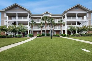 A multi-story hotel with balconies, a central courtyard, and palm trees. - A Breath of Myrtle Retreat (North Myrtle Beach)