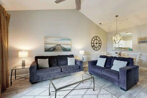 A living room with two sofas, a coffee table, a painting, a clock, and a chandelier. - A Breath of Myrtle Retreat (North Myrtle Beach)