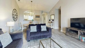 Ein modernes Wohnzimmer mit grauem Sofa, einem Flachbildfernseher und einer Kristallleuchter.