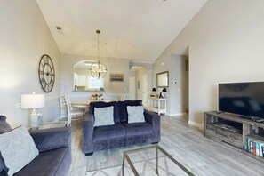 A modern living room with a grey sofa, a flat-screen TV, and a chandelier. - A Breath of Myrtle Retreat (North Myrtle Beach)