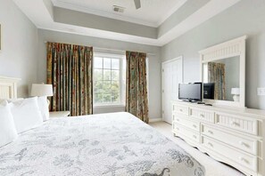 Une chambre à coucher avec un grand lit, un téléviseur posé sur une commode et une fenêtre avec des rideaux.