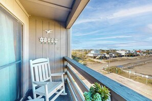 A balcony with a white rocking chair and a potted plant, overlooking a parking lot and buildings. - Garden City Dreaming (Garden City Beach)