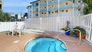 En swimmingpool med ett vitt staket, en vit byggnad med balkonger och krukväxter.