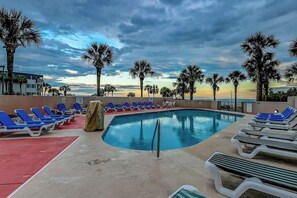 A pool area with lounge chairs, palm trees, and a sunset view. - Ocean Forest Plaza 1213 (Myrtle Beach)