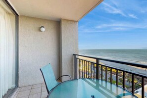 A balcony with a glass table and chair, overlooking a body of water. - Ocean Forest Plaza 1213 (Myrtle Beach)