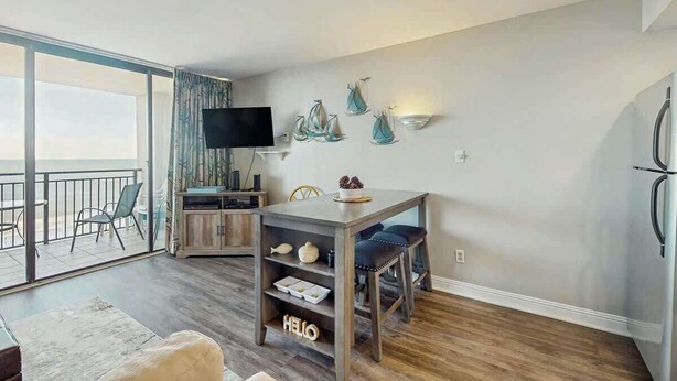 Ein modernes Wohnzimmer mit Flachbildfernseher, einem Essbereich mit Holztisch und Stühlen sowie einem Balkon mit Aussicht.