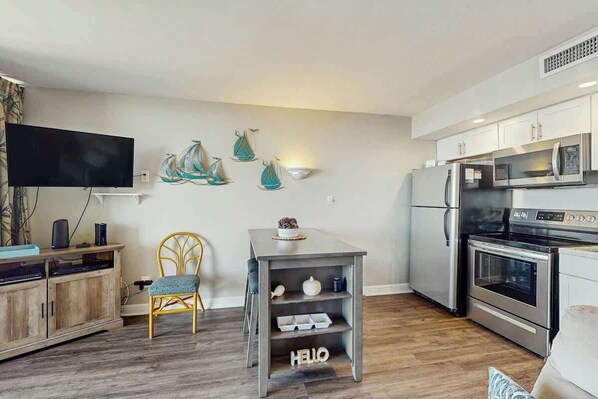A modern kitchen with stainless steel appliances, a flat-screen TV, and decorative wall art. - Ocean Forest Plaza 1213 (Myrtle Beach)