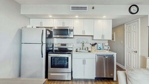 Eine kompakte Küche mit weißen Schränken, einem Kühlschrank, einer Mikrowelle, einem Backofen und einem Geschirrspüler.