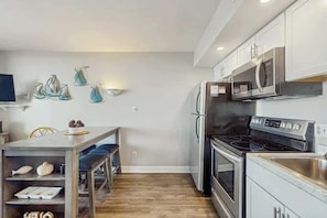 A modern kitchen with a wooden dining table, stainless steel appliances, and decorative wall art. - Ocean Forest Plaza 1213 (Myrtle Beach)