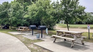 Ein Picknickbereich im Freien mit Holztischen und Grillmöglichkeiten, umgeben von Bäumen.
