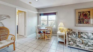 A living room with a dining table, chairs, a sofa, and a window with a view. - Live in the Sun, Play in the Sea (Surfside Beach)