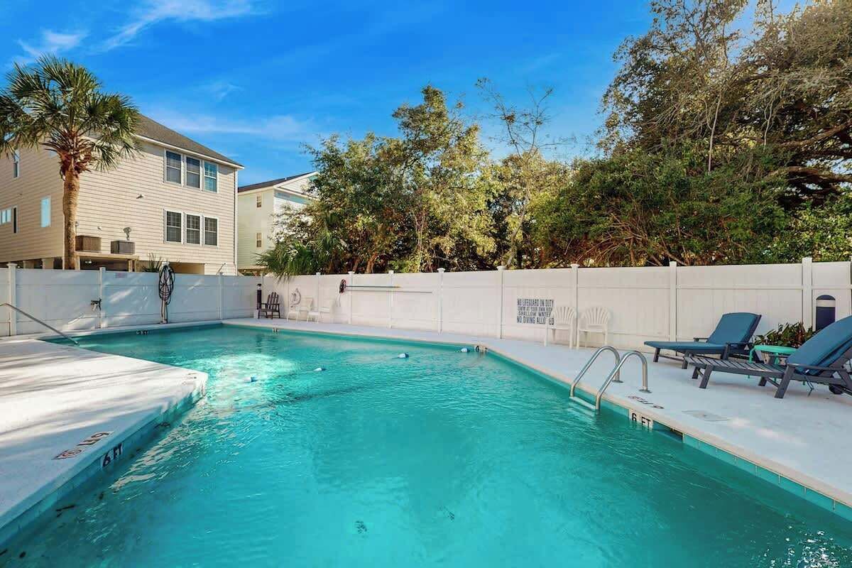 A swimming pool with a white deck, lounge chairs, and a white fence.