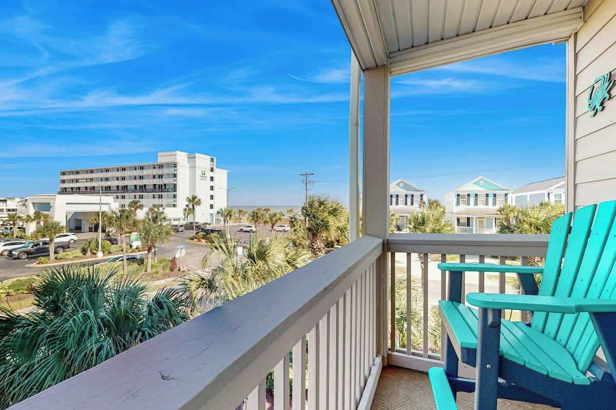 A balcony with a view of a building complex, a parking area, and palm trees.