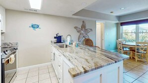 A kitchen with a marble countertop, a sink, and a dining area with a table and chairs. - Live in the Sun, Play in the Sea (Surfside Beach)