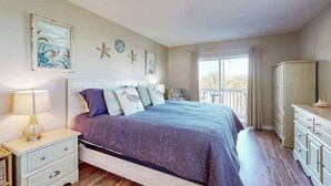 A bedroom with a bed, a nightstand, a dresser, and a window with curtains. - Live in the Sun, Play in the Sea (Surfside Beach)