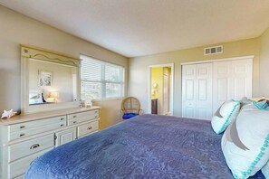 Ein Schlafzimmer mit Bett, Kommode, Spiegel und einer Tür zu einem anderen Raum.