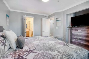 Ein Schlafzimmer mit Bett, Kommode, Fernseher und einer Tür zu einem anderen Raum.