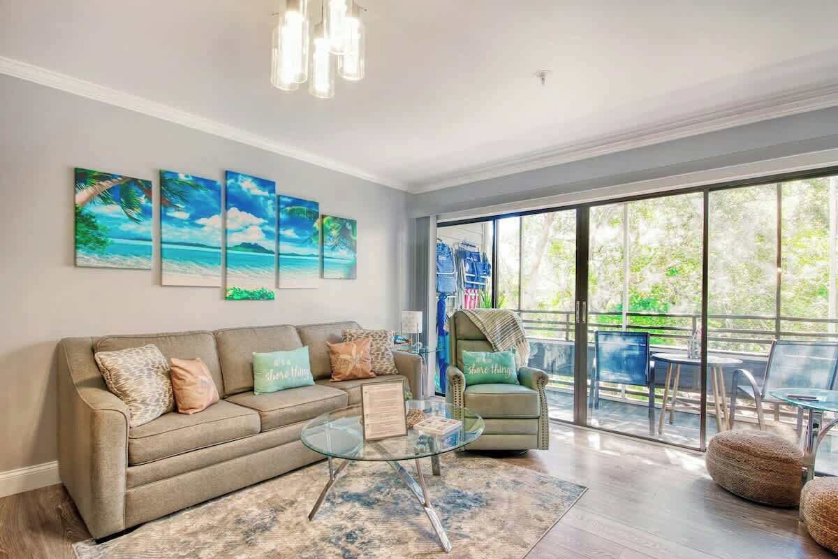 A living room with a sofa, a glass coffee table, and a view of the outdoors through large windows.