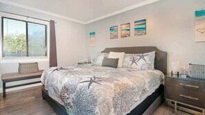 Une chambre à coucher avec un grand lit, un banc, une table de chevet et des œuvres d’art accrochées au mur.