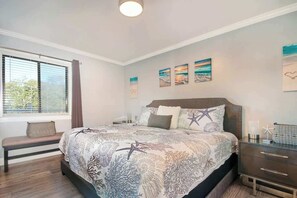 A bedroom with a large bed, a bench, a bedside table, and artwork on the wall. - Sand Angels at Ocean Creek (Myrtle Beach)
