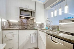 A modern kitchen with a microwave, dishwasher, and a tiled backsplash. - Sand Angels at Ocean Creek (Myrtle Beach)