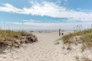 A sandy beach with a clear sky and a few people in the distance. - Sand Angels at Ocean Creek (Myrtle Beach)