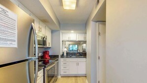 A modern kitchen with stainless steel appliances, white cabinetry, and a wooden floor. - Summertree Village A-11 (Myrtle Beach)