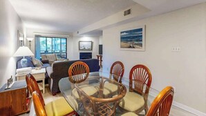 A living room with a glass dining table surrounded by wooden chairs, a sofa, and a lamp. - Summertree Village A-11 (Myrtle Beach)