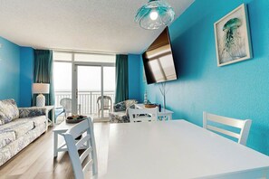 A room with a white table, chairs, a sofa, and a TV mounted on the wall.