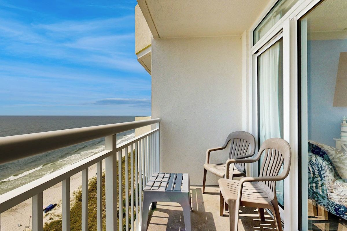 A balcony with a view of the ocean, two chairs, and a small table.