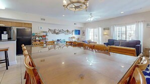 A spacious living area with a large dining table, a kitchen with modern appliances, and a ceiling fan. - Coconut Grove Unit 202 (North Myrtle Beach)