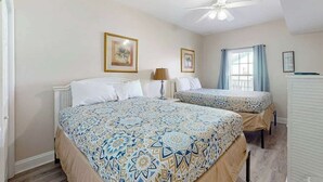 A bedroom with a bed, a bedside table, a lamp, and a window with curtains. - Coconut Grove Unit 202 (North Myrtle Beach)