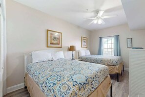 A bedroom with a bed, a bedside table, a lamp, and a window with curtains. - Coconut Grove Unit 202 (North Myrtle Beach)