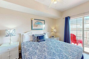 A hotel room with a bed, a nightstand, a lamp, a framed picture on the wall, and a view of the outside. - Coconut Grove Unit 202 (North Myrtle Beach)