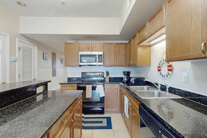A kitchen with wooden cabinets, a microwave, an oven, and a coffee maker. - Coconut Grove Unit 202 (North Myrtle Beach)