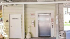 A private property entrance with a fire alarm room door, a sprinkler room door, and a trash bin. - Coconut Grove Unit 202 (North Myrtle Beach)