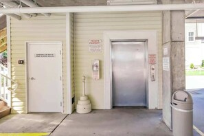 A private property entrance with a fire alarm room door, a sprinkler room door, and a trash bin. - Coconut Grove Unit 202 (North Myrtle Beach)