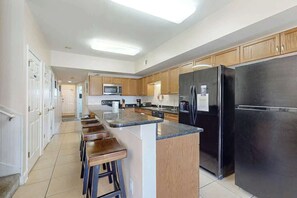 A spacious kitchen with a central island, wooden cabinets, stainless steel appliances, and a long countertop. - Coconut Grove Unit 202 (North Myrtle Beach)