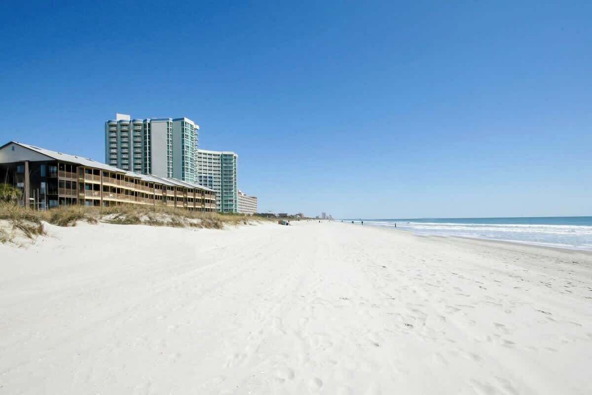 A beach with a hotel building and a high-rise building in the background.