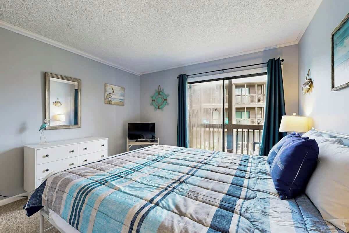 A bedroom with a bed, a dresser, a television, and a window with curtains.