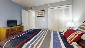 A bedroom with a bed, a dresser, a television, a closet, and a painting on the wall. - Tilghman Beach & Racquet 214 (North Myrtle Beach)