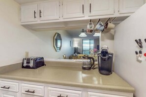 A kitchen with white cabinets, a toaster, a coffee maker, and a mirror. - Holiday Towers Unit 1001 (Myrtle Beach)
